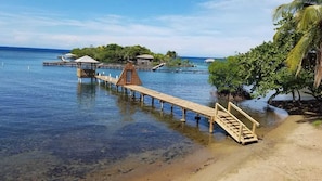 A wooden pier extending into calm waters, leading to a small wooden structure with a thatched roof. - Beachfront Cabana - Ocean Views - A/C Included - Full Kitchen - Snorkeling (Sandy Bay)