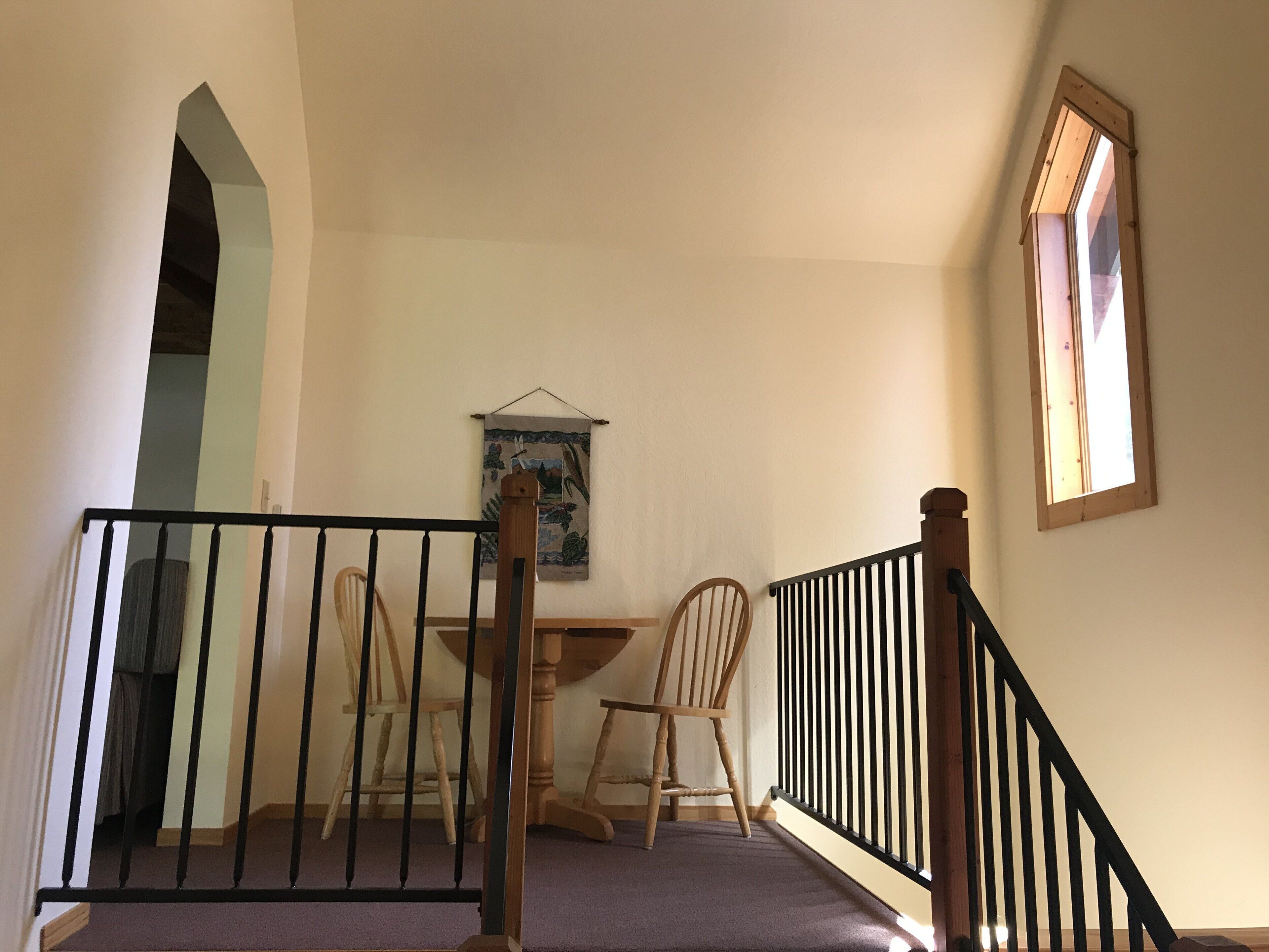 Un escalier doté d’une rampe en bois et de balustres noires, menant à une pièce où se trouvent une table à manger et deux chaises.