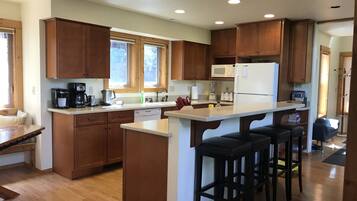 Une cuisine moderne avec des meubles en bois, un îlot central doté de tabourets, un four à micro-ondes et un réfrigérateur.