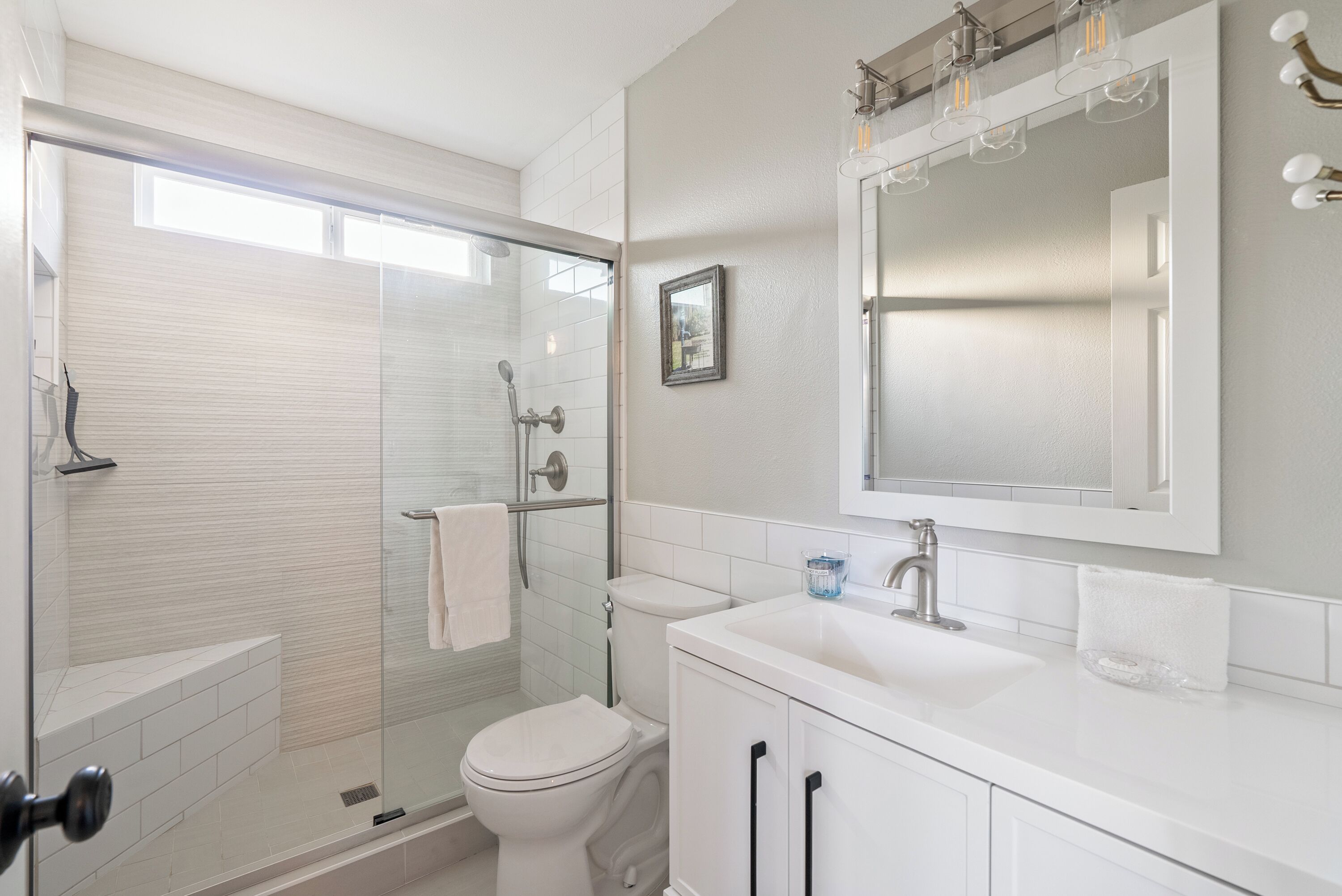 Une salle de bain moderne avec une douche à parois de verre, des toilettes, un lavabo avec un miroir au-dessus et un porte-serviettes.