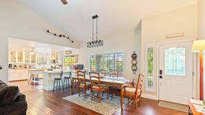 A spacious kitchen with white cabinets, a dining area with wooden chairs, and a large window. - Waterfall Spa + Sunset Views | Atascadero Wine Country | Summer Place (Templeton)
