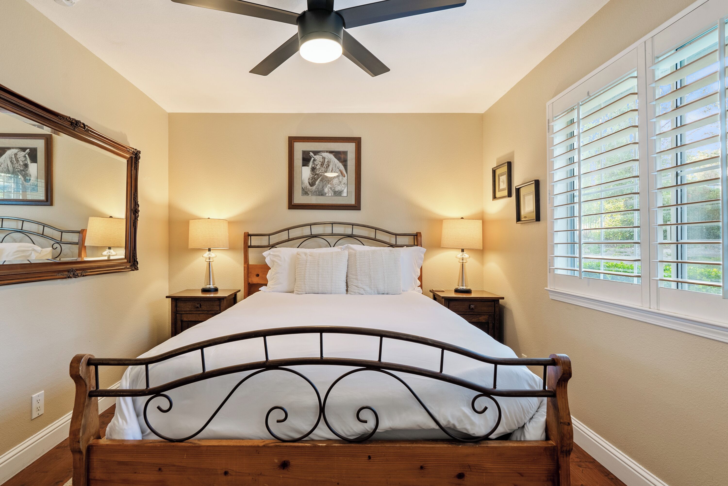 A bedroom with a bed, two bedside tables, a ceiling fan, and a window with blinds.