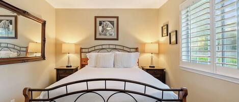 A bedroom with a bed, two bedside tables, a ceiling fan, and a window with blinds.