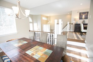 Un coin repas avec une table en bois, des chaises et un lustre. Un escalier mène à un autre niveau.