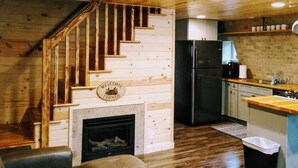 Interior de madera con escalera, refrigerador negro y chimenea.