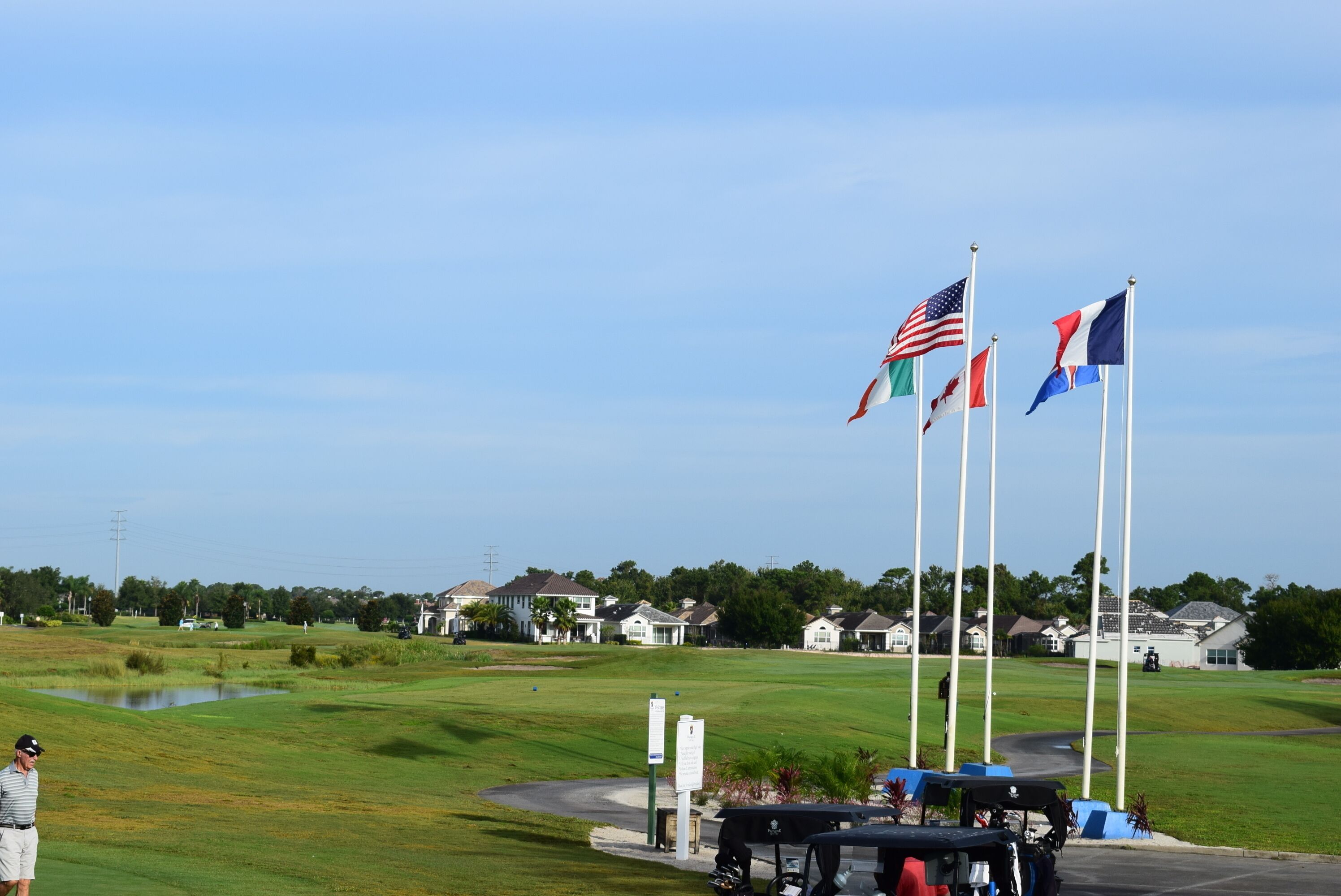 Un terrain de golf avec des drapeaux, un étang et des maisons en arrière-plan.