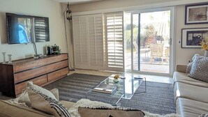 Ein Wohnzimmer mit einer Couch, einem Couchtisch und einem Fernseher. Eine Glastür führt in einen Außenbereich.