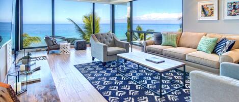 A spacious living room with a large window offering a view of the ocean, a ceiling fan, and a modern sofa set.