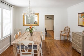 Une salle à manger avec une table en bois, des chaises blanches, un lustre et un miroir au mur.