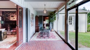 A covered patio with a brick floor, a glass table with chairs, and a hanging light fixture. - Bayou Liberty Waterfront Estate (Slidell)