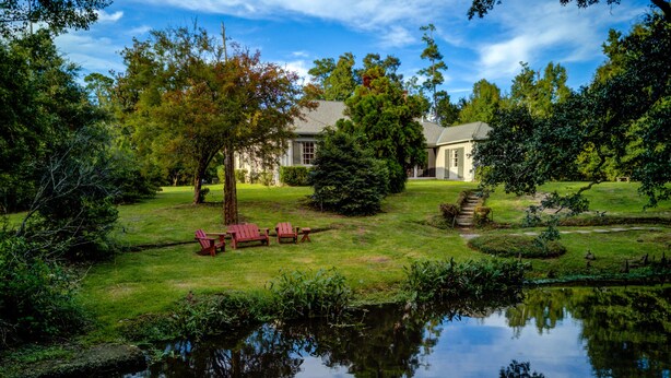A house with a pond in front, surrounded by trees and a lawn. - Bayou Liberty Waterfront Estate (Slidell)