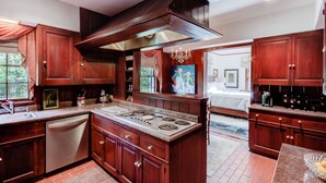 A spacious kitchen with wooden cabinets, a central island stove, and a chandelier. - Bayou Liberty Waterfront Estate (Slidell)