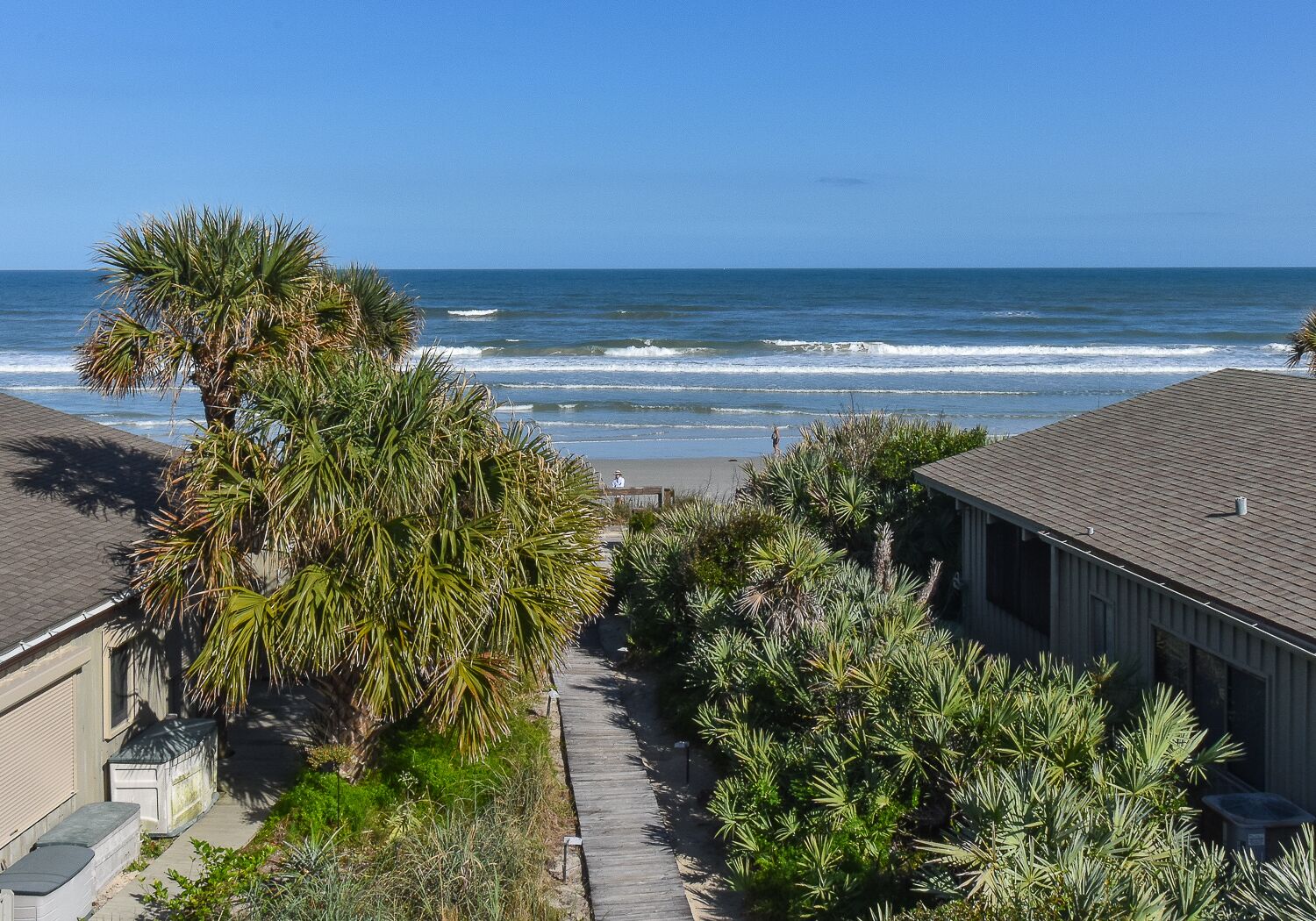 A coastal residential area with a view of the ocean, a wooden pathway, and houses with a beach in the background.