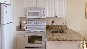 Una cocina compacta con armarios blancos, microondas integrado, estufa y refrigerador.