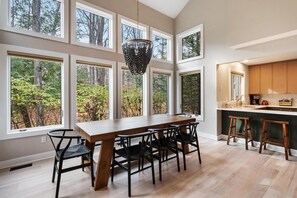 A modern kitchen with large windows, a wooden dining table, and black chairs.