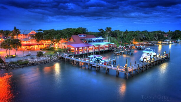 A waterfront property with a dock, boats, and a building with a red roof and illuminated windows. - Getaway New Smyrna Beach, Sun, Pool, Shopping. (New Smyrna Beach)
