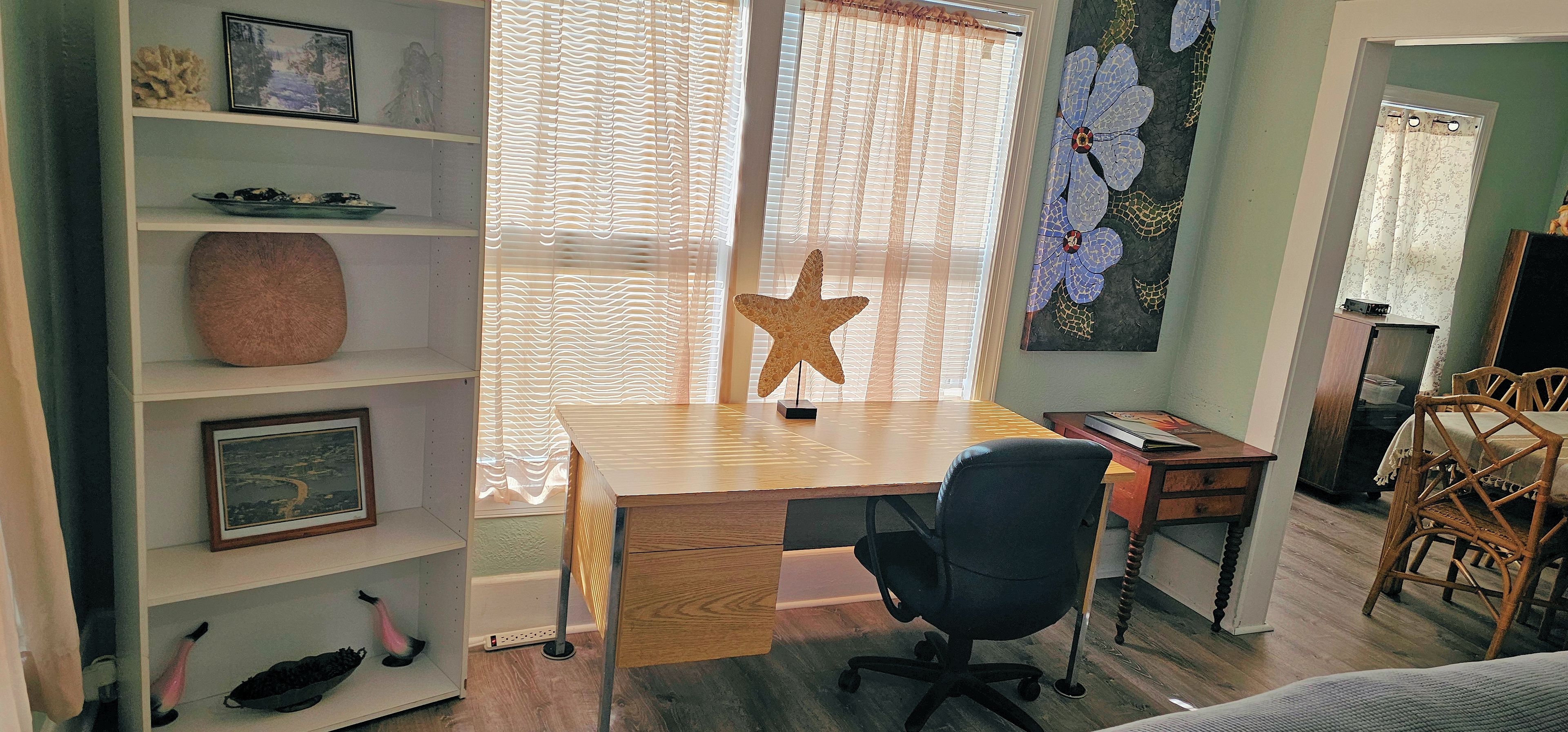 A room with a wooden desk, a black office chair, a starfish decoration, and a bookshelf with various items.