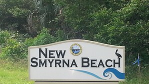 A sign for New Smyrna Beach with a logo and a bird illustration. - Getaway New Smyrna Beach, Sun, Pool, Shopping. (New Smyrna Beach)
