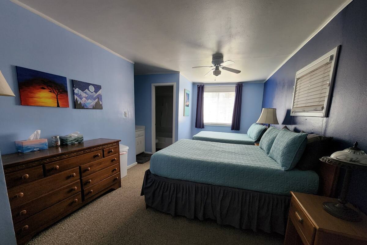A bedroom with a bed, dresser, ceiling fan, and artwork on the wall.