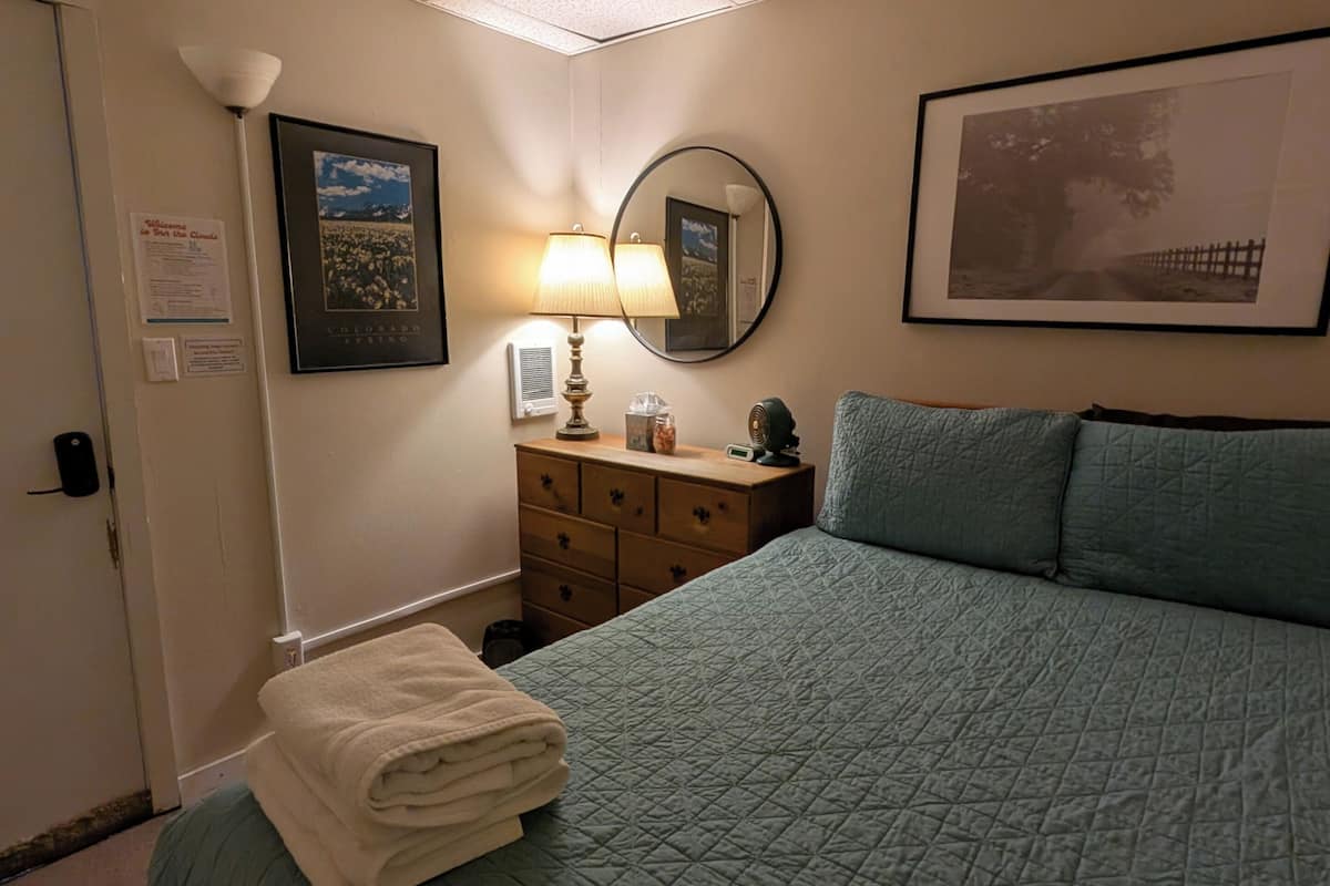 A hotel room with a bed, a dresser, a lamp, a framed picture, and a mirror.