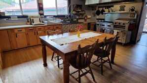 A kitchen with wooden cabinets, a dining table with chairs, a vase with flowers, and a stove. - Inn the Clouds Hostel & Inn (Leadville)