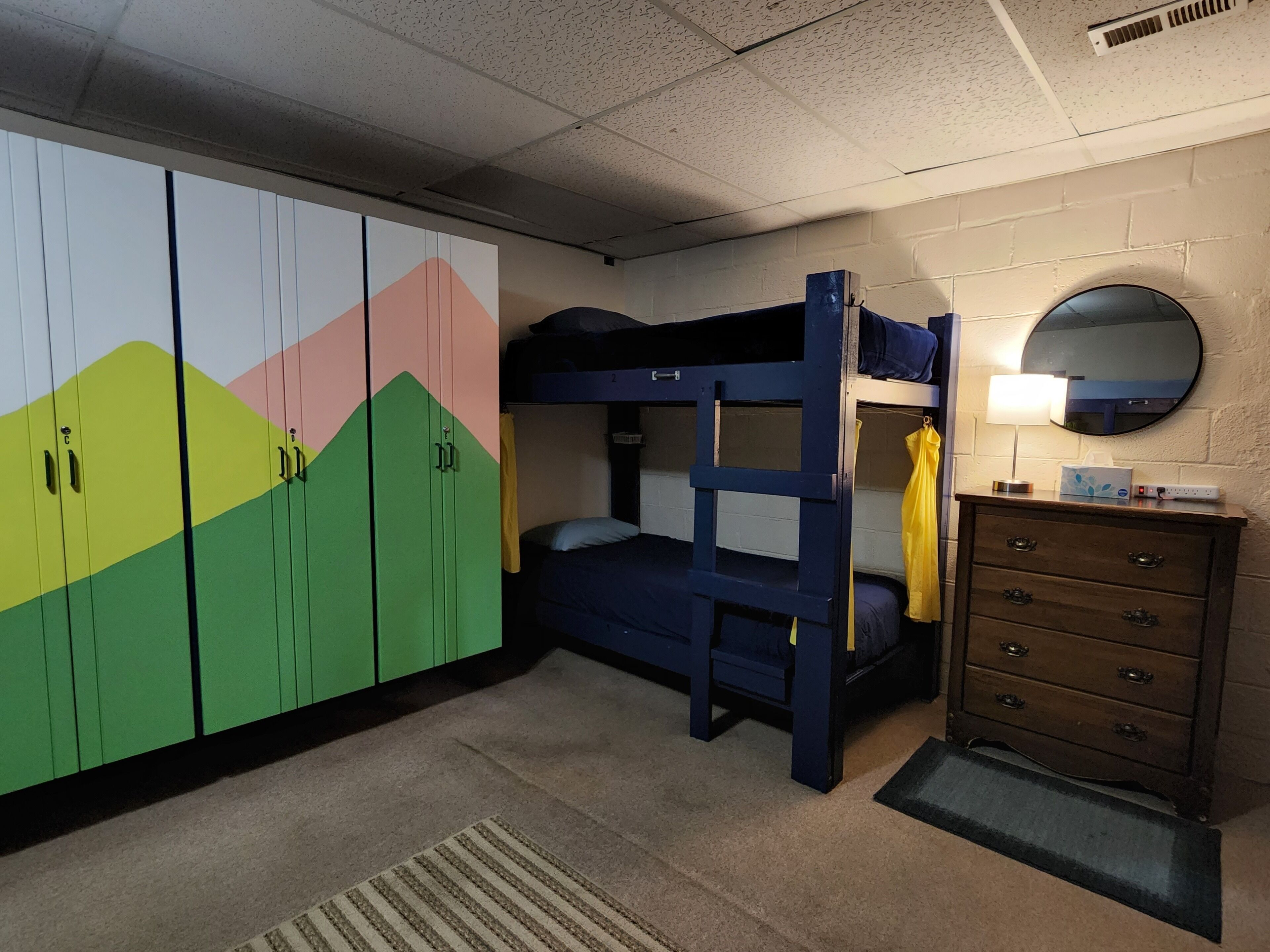 A bunk bed with a dresser and a mirror. There is a wardrobe with colorful doors.