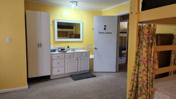 A bathroom with a sink, mirror, and cabinets. There is a door labeled "Twin Lakes" and a shower curtain with a floral pattern.