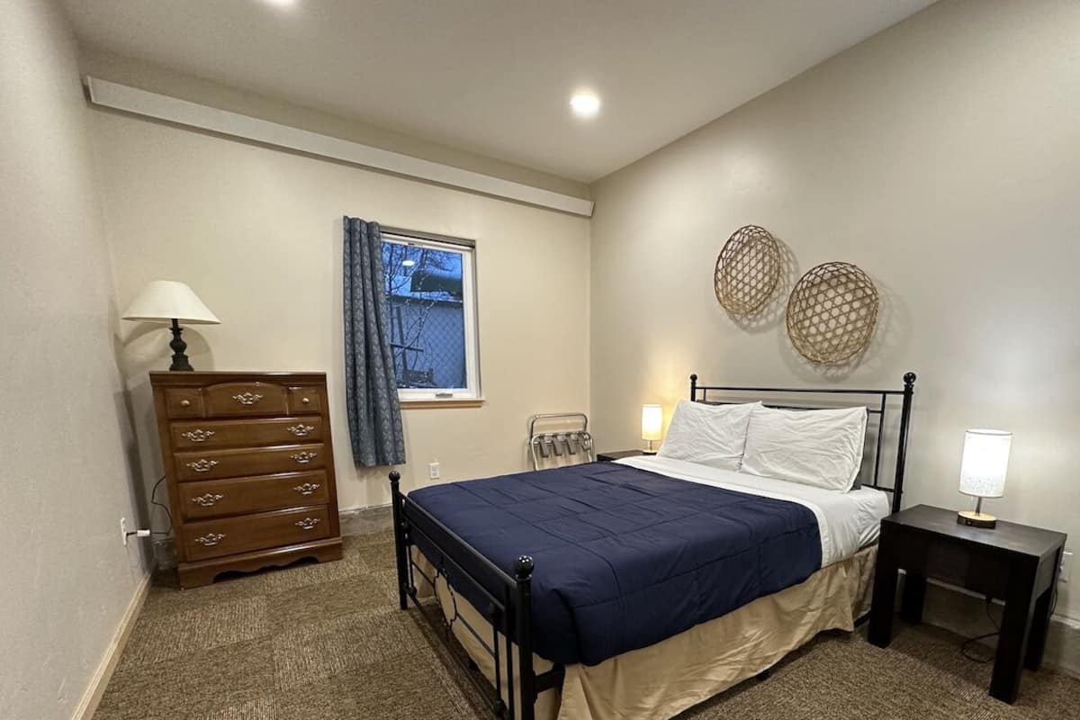 A bedroom with a bed, dresser, bedside lamps, and decorative wall art.