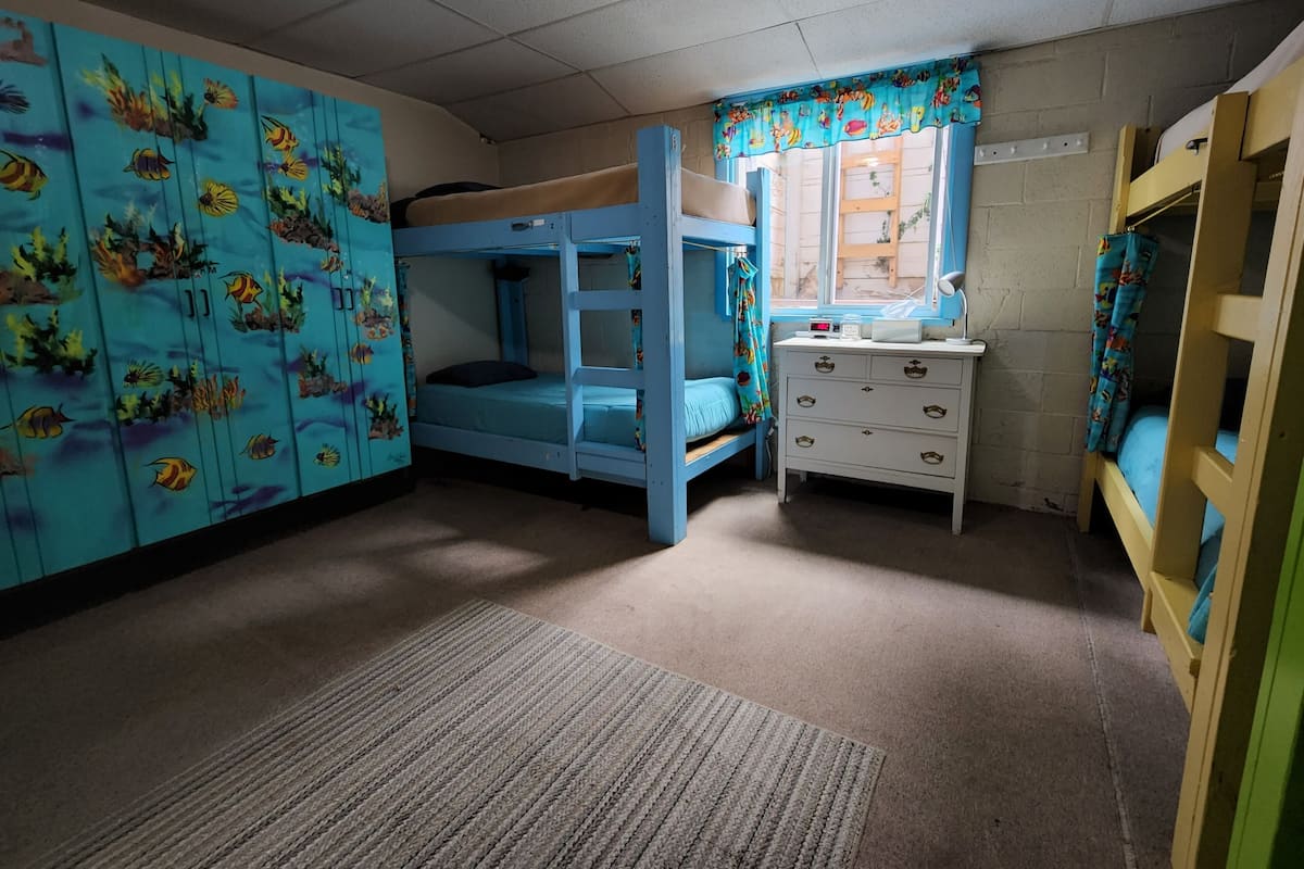 A bunk bed room with a blue theme, a dresser, and a window with a curtain.