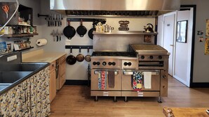 A kitchen with a stainless steel range, hanging pots, and a wooden counter with a floral pattern. - Inn the Clouds Hostel & Inn (Leadville)