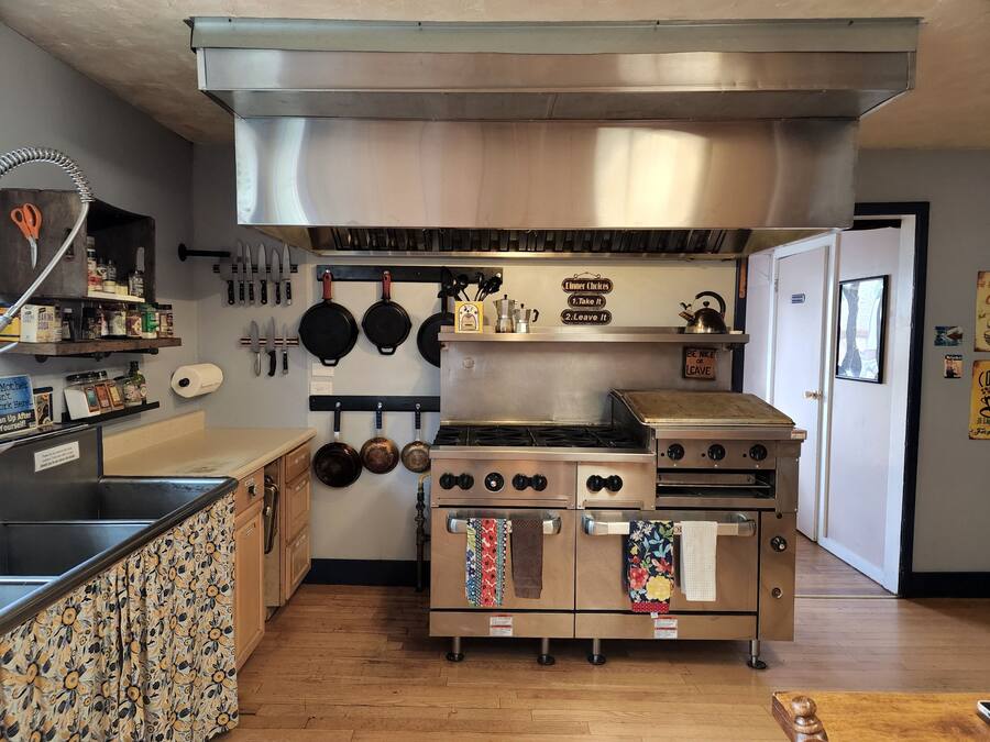 Una cocina con estufa de acero inoxidable, ollas colgantes y encimera de madera con estampado floral.
