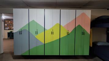 Ein Schlafsaalzimmer mit Etagenbetten, einem Kleiderschrank mit bunten Berggrafiken und einer Pinnwand in der Ecke.