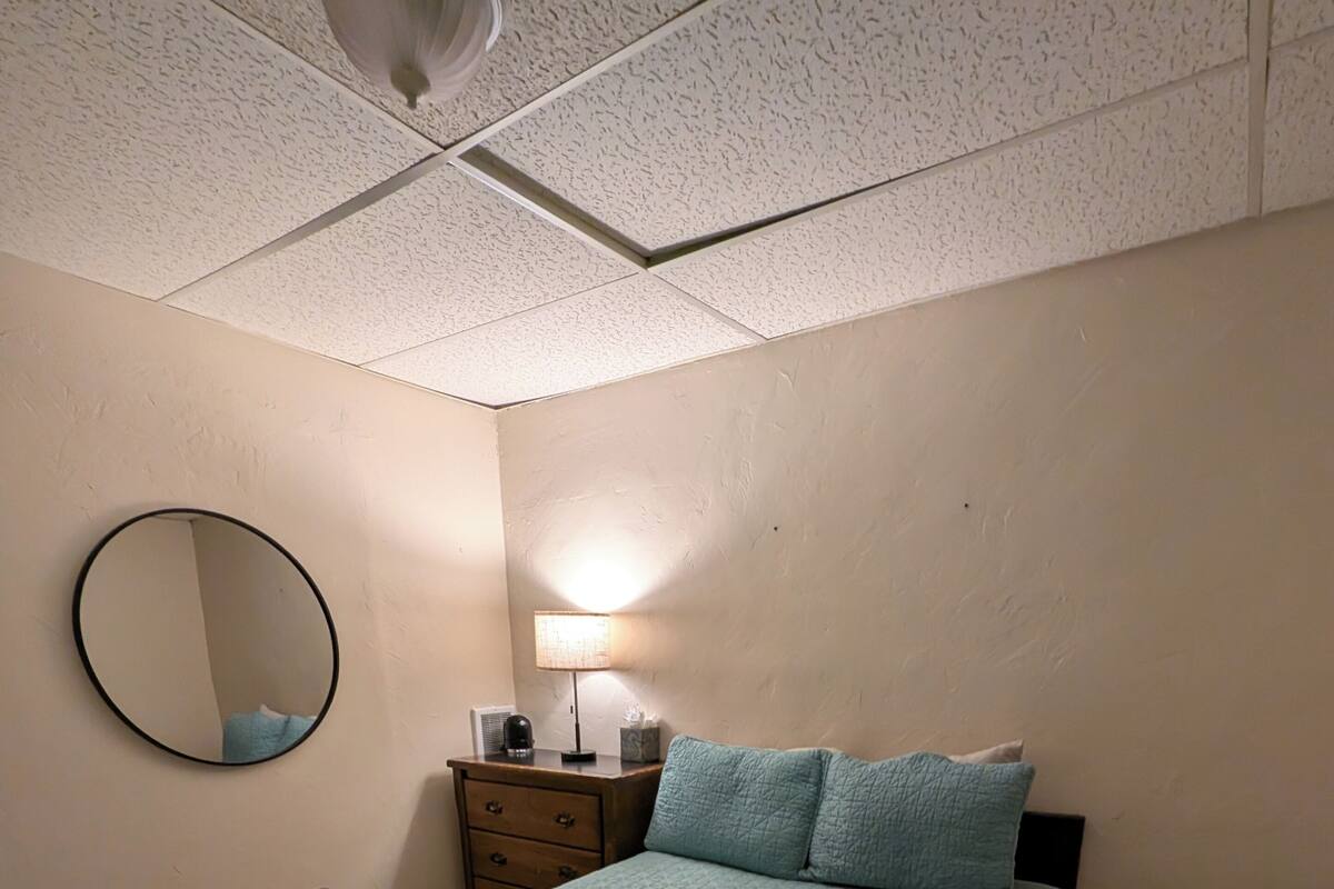 A bedroom with a bed, a round mirror, a bedside table with a lamp, and a small rug.