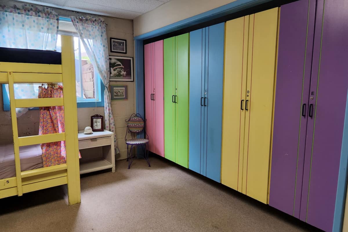A room with bunk beds, a small desk, a chair, and colorful lockers.
