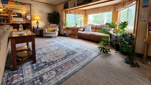 A cozy living room with a sofa, armchair, and coffee table, a rug, and a window with a view of trees. - Inn the Clouds Hostel & Inn (Leadville)