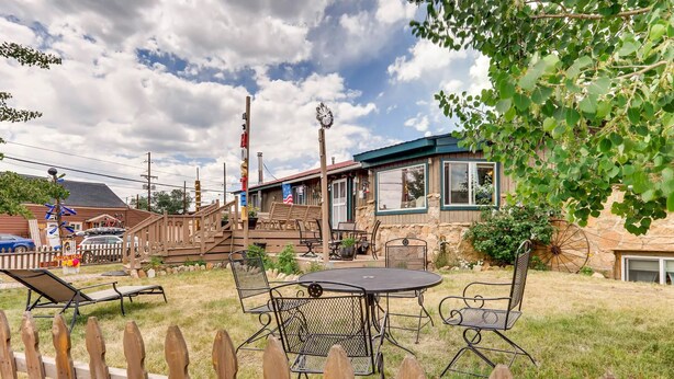 A backyard with a patio table and chairs, a wooden deck, and a stone building with windows. - Inn the Clouds Hostel & Inn (Leadville)