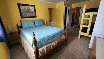 Un dormitorio con cama de madera, ventilador de techo, un cuadro en la pared y una puerta que da a otra habitación.