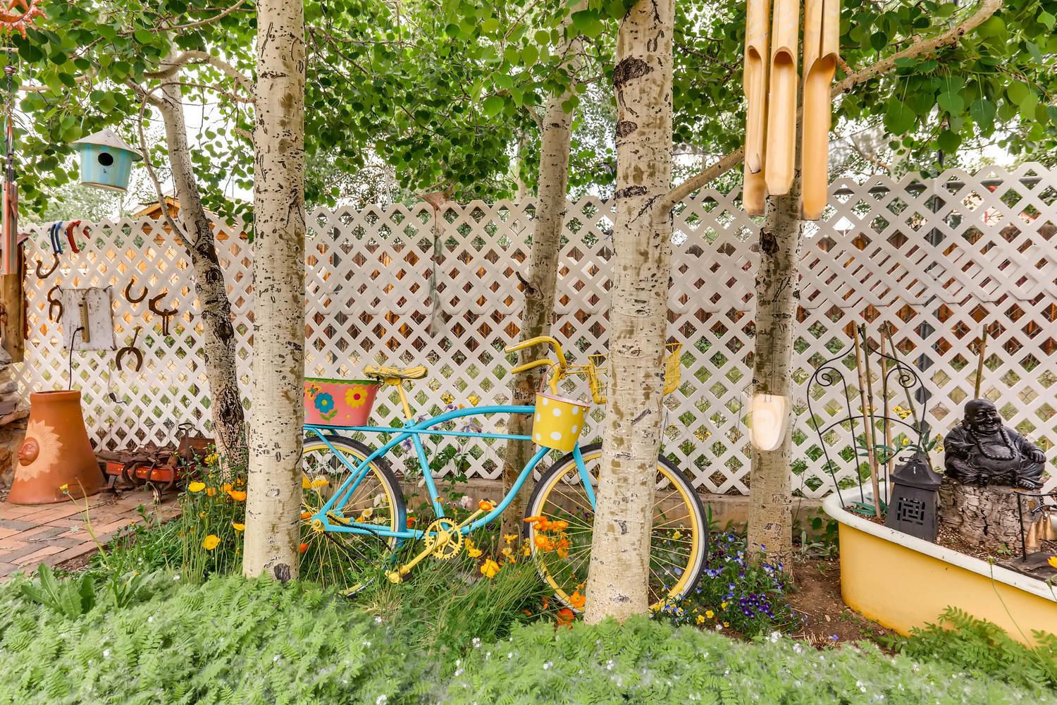 Un jardín con una bicicleta, un comedero para pájaros y una estatua.