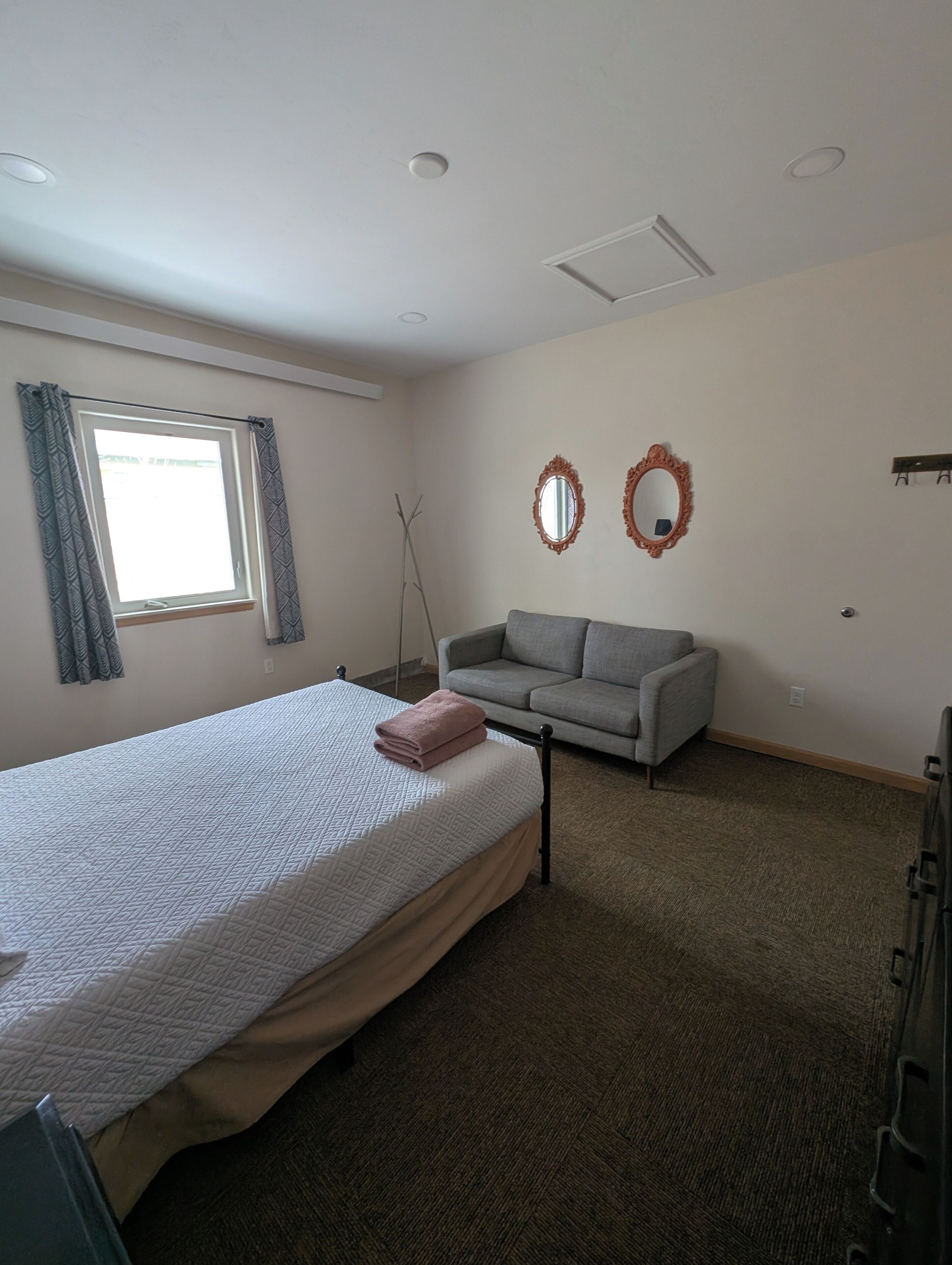 A room with a bed, a grey sofa, two wall-mounted mirrors, a window with curtains, and a radiator.