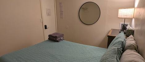 Una habitación de hotel con una cama, un espejo redondo, una lámpara y una puerta.