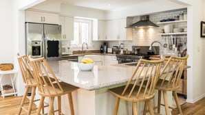 Una cocina moderna con armarios blancos, un refrigerador de acero inoxidable, una isla grande con taburetes de bar y una suspensión para colgar ollas.