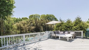 Una terraza de madera con mobiliario exterior, incluyendo un sofá y una mesa, rodeada por una barandilla blanca.