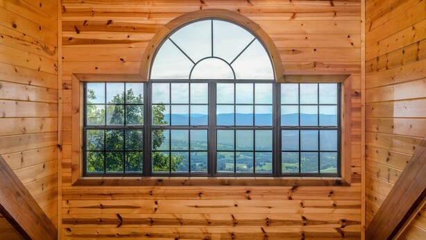 Una baita di legno con un'ampia finestra ad arco che si affaccia sul paesaggio.