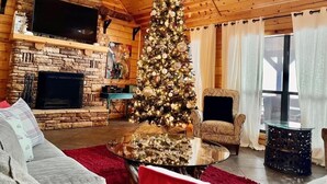 Un accogliente interno di una baita con un camino in pietra, un albero di Natale, una televisione e un’area salotto confortevole.