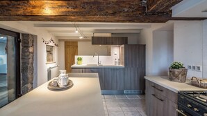 A modern kitchen with a central island, wooden ceiling beams, and a stone accent wall. - High standing Vosges farmhouse, Les Bois du Cerf (Gérardmer)