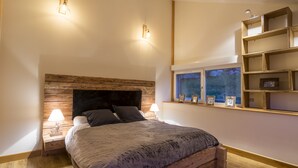 A bedroom with a wooden headboard, a large bed, bedside lamps, a window with a view, and built-in shelves. - High standing Vosges farmhouse, Les Bois du Cerf (Gérardmer)
