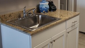 Eine Küche mit weißen Schränken, einer Granit-Arbeitsplatte, einer Spüle, einem Mixer und einer dekorativen Glasvase.