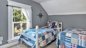 A bedroom with a window, a compass wall decoration, a bed with a quilt, and a USA-themed pillow. - Welcome Home (+ your pup) MSU 2 mi (Lansing)