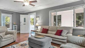 A living room with a sofa, ottoman, and armchair, a ceiling fan, and a door leading outside. - Welcome Home (+ your pup) MSU 2 mi (Lansing)