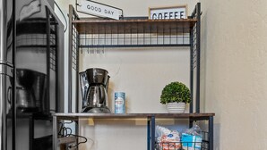 Une petite cuisine équipée d’une machine à café, d’une étagère ornée d’une enseigne sur le thème du café et d’une petite plante.